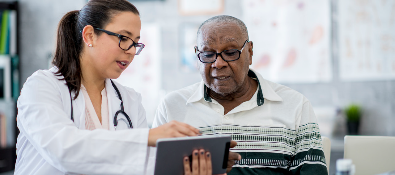 Healthcare professional assisting a patient while looking at a tablet