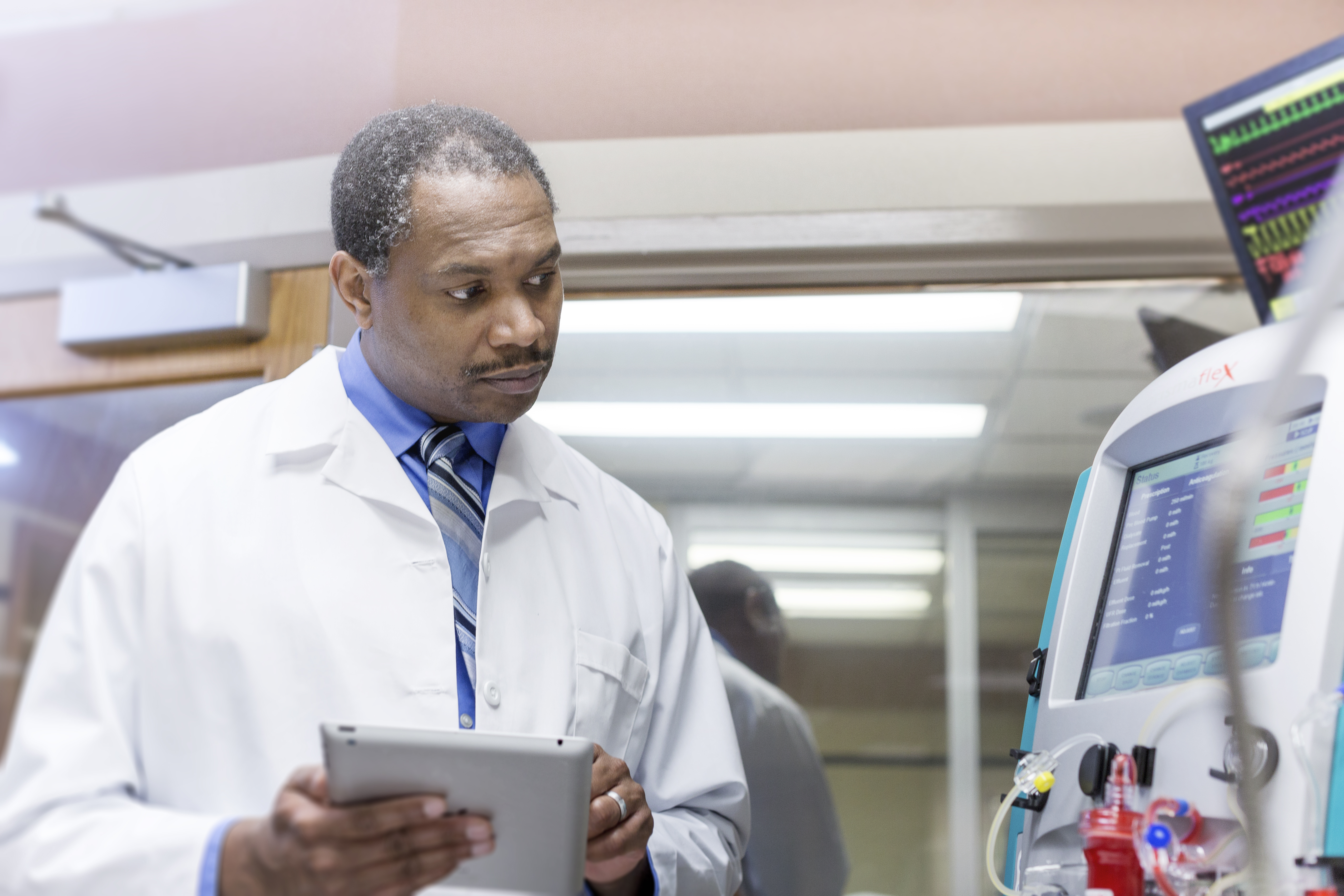 Doctor holds tablet and analyzes at data from the PRISMAFLEX System CRRT machine.